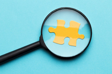 Magnifying glass over yellow puzzle piece on blue backdrop