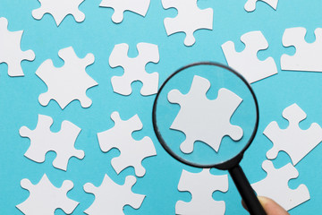 White jigsaw piece seen through magnifying glass over blue white background
