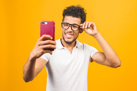 Image of happy young african american man posing isolated over yellow background take a selfie by phone.