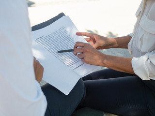 Female business colleagues examining contract text. Anonymous business women sitting outdoors, reading document and pointing pen at text. Expertise and paperwork concept