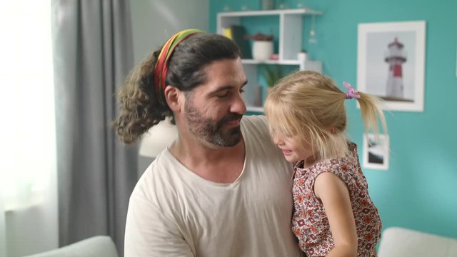 Dad is dancing with his daughter in his arms at home