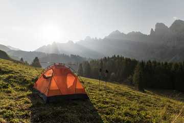 Beautiful early morning camping view. Dolomites sunrise landscape with an orange trekking tent