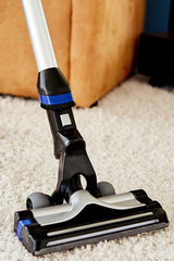 Close up of modern vacuum cleaner on beige carpet on floor in living room, copy space. Housework, household, spring-cleaning and chores concept. House cleaning