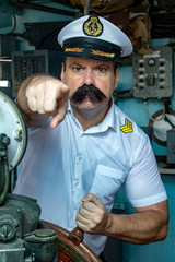 A sailor officer in the uniform is steering the ship with a rudder. Captain in the wheelhouse pointing his finger ahead to camera. © milkovasa