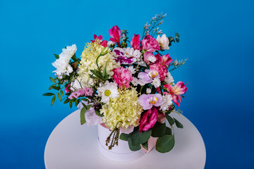 Beautiful bouquet of flowers on white round table on blue background.