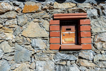 Close-up of an old and rusty metal mailbox embedded in the stone wall. Liguria, Italy