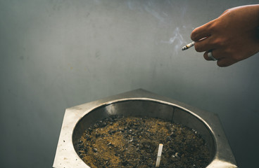 Closeup hand of a man with cigarette. People smoking in smoking zone area of the mall and left...
