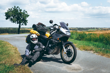 Obraz premium Mężczyzna kierowca w płaszczu przeciwdeszczowym siedzi przy motocyklu przygodowym z bocznymi torbami. wycieczka motocyklowa. Czas letni na zewnątrz drogi. Świat podróż na dwóch kołach, koncepcja wolności. wyposażenie jeźdźca.