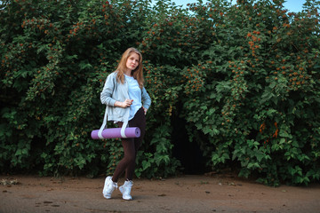 Fitness woman carrying yoga mat with strap on vegetative background