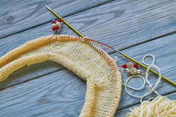 Yellow knitted handmade raglan or jumper on blue wooden background. Work in progress. Closeup