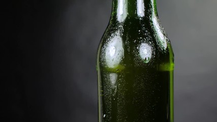 A green bottle of freshly brewed cold beer on a black background. A ray of light beautifully illuminates it. It slowly rotates.