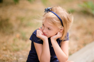 Adorable blonde brown-eyed girl dreams in the park. Warm green background