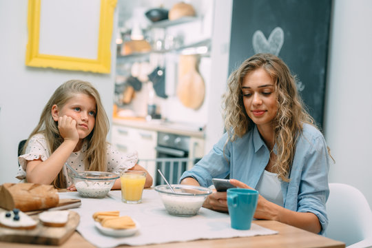 daughter is borred while mother talking on mobile phone during breakfast at home