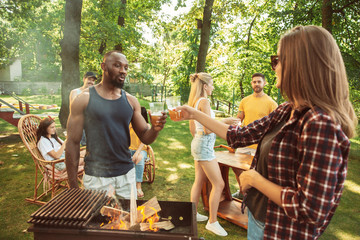 Naklejka na ściany i meble Group of happy friends having beer and barbecue party at sunny day. Resting together outdoor in a forest glade or backyard. Celebrating and relaxing, laughting. Summer lifestyle, friendship concept.