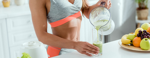 panoramic shot of girl holding glass while pouring smoothie from blender