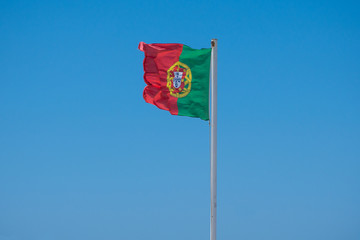 Flag of Portugal flying against blue sky, blowing in wind.