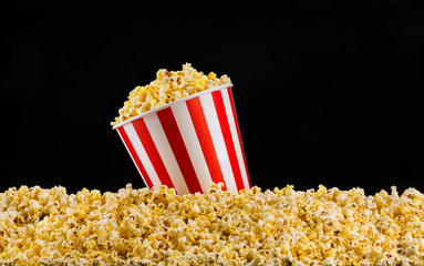 Paper striped bucket installed on scattered popcorn isolated on black background