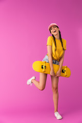 Full length image of delighted caucasian woman wearing cap smiling and holding skateboard