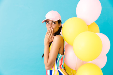 Image of alluring woman wearing cap looking aside at copyspace and covering her mouth while holding...