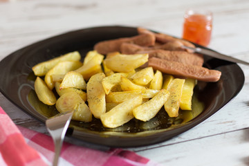 French fried potatoes on black plate with sauce on wooden table. Tasty french fries. Baked potatoes by slices.