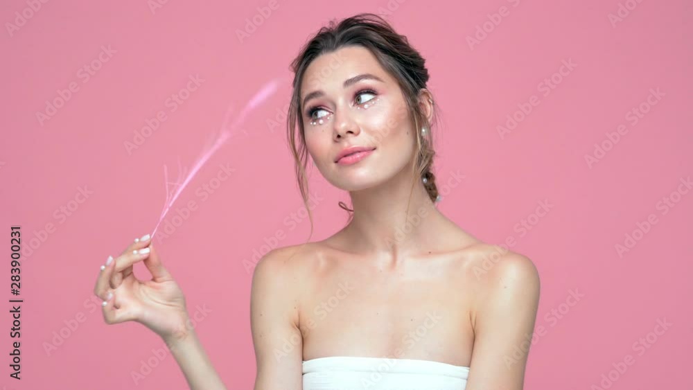 Sticker Beauty playful brunette woman with pearls on face and hands posing with peather over pink background