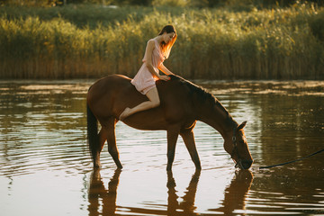 Woman sits astride a horse that drinks water.