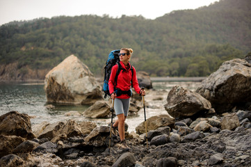 Slim fit woman standing on the rocks on the coastline on the sea with hiking backpack