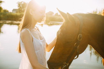 Woman stands next to horse on river at sunset.