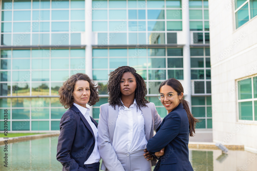 Wall mural Team portrait of three successful businesswomen. Women wearing office suits, standing together outside and looking at camera. Female business team concept