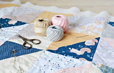 Hand stitch quilting process: cotton thread, needle and scissors on the table	