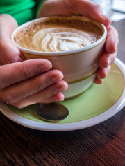 blurred Female hand holding cup of coffee on wooden background