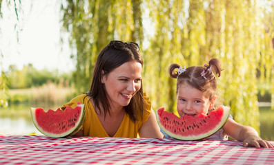 Mother and daughter eating watermelon slice on a picnic In a park
