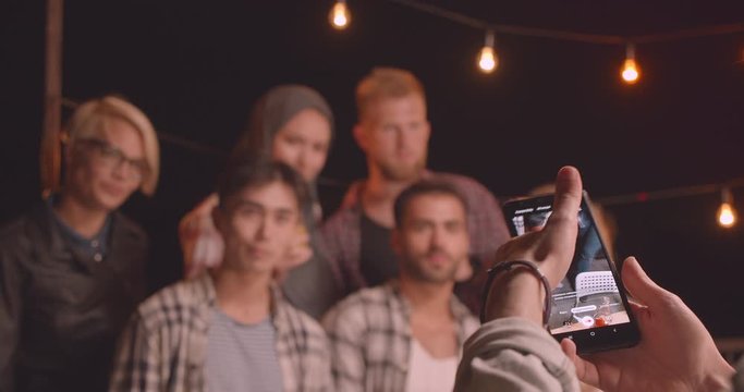 Closeup portrait of diverse multiracial group of friends being photographed on instagram camera at fun party in cozy evening