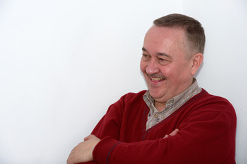 Close-up half length portrait of laughing  mature man in red pullover on white wall background.