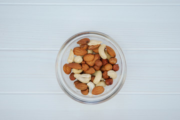 Assorted nuts in a glass bowl on a white wooden background, top view