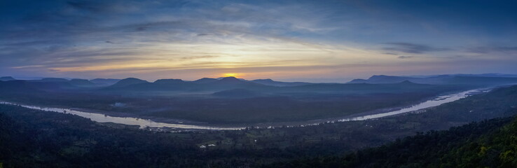 Top view panorama of Mekong river around with soft mist, forest, mountains with cloudy and yellow sun light in the sky background, sunrise at Cha Na Dai Cliff, Ubon Ratchathani, Thailand.