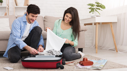 Loving couple packing clothes into suitcase at home