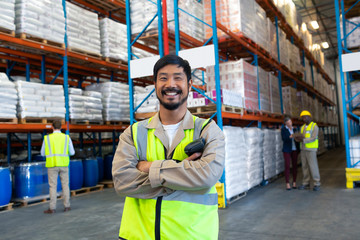 Male worker standing with arms crossed and looking at camera in warehouse