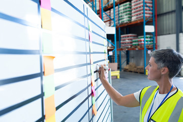 Female staff writing on whiteboard in warehouse