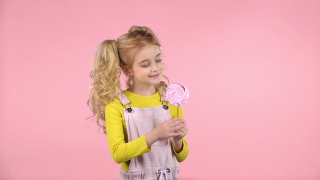Pretty girl is looking at pink candy on stick. Slow motion