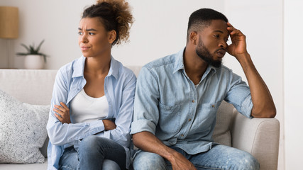 Sad african american couple sitting on couch looking away