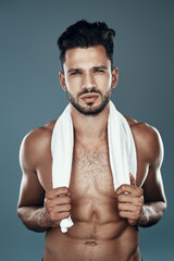 Handsome young shirtless man looking at camera while standing against grey background