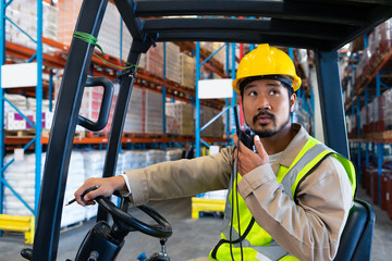 Male worker talking on walkie-talkie while driving forklift in warehouse