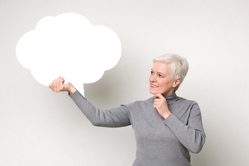Senior female holding blank speech bubble on light studio background
