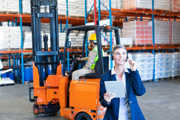 Female manager with digital tablet talking on headset in warehouse