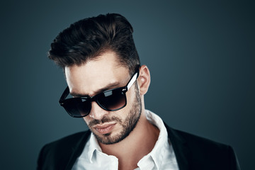 Obraz premium Charming young man in eyewear looking down while standing against grey background