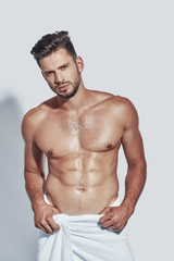 Handsome young shirtless man looking at camera while standing against grey background