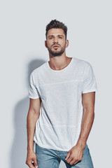 Handsome young man looking at camera while standing against grey background