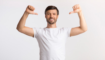 Positive Man Pointing With Thumbs At Himself Over White Background