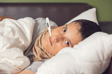 Sick boy with thermometer laying in bed. Sick child with fever and illness in bed. Flu. Cold